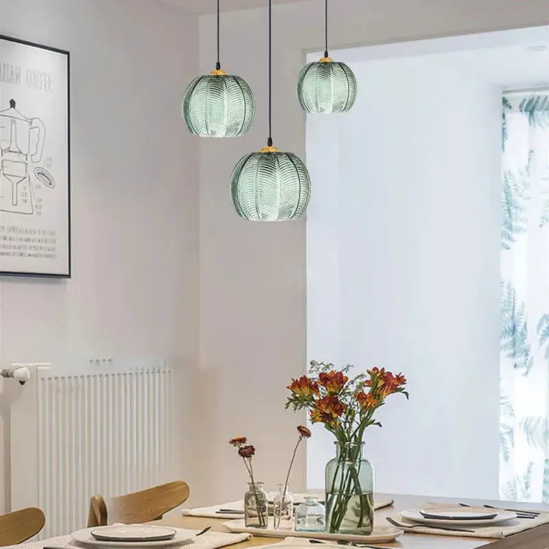Nordic glass pendant lights in green with leaf pattern, three hanging above a dining table.