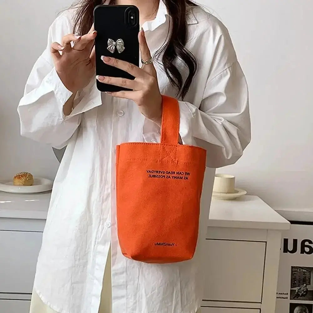 Orange canvas tote bag with short handles, carried by a person wearing a white shirt