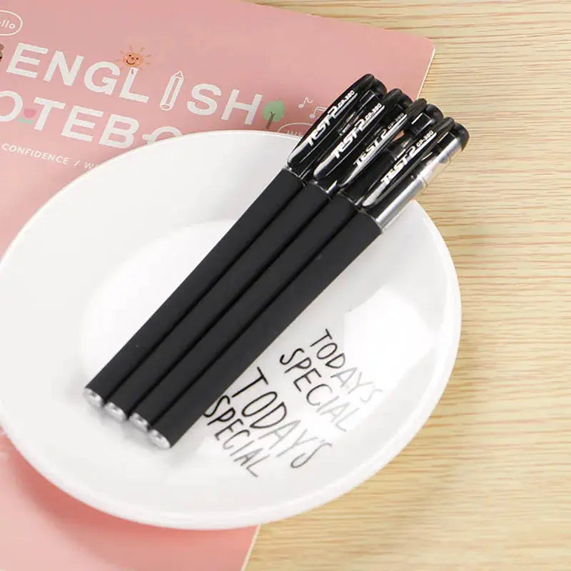 Gel pen set, five black gel pens on a white plate beside a pink notebook
