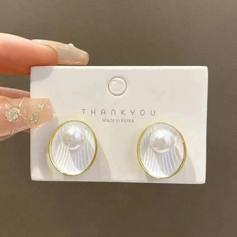 Gold-tone circular stud earrings with white faux pearl accents on a display card