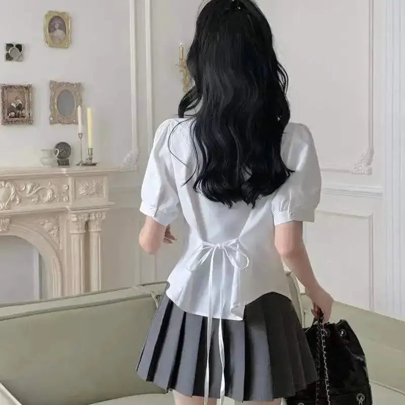 White blouse with back tie and puff sleeves, paired with a gray pleated skirt.