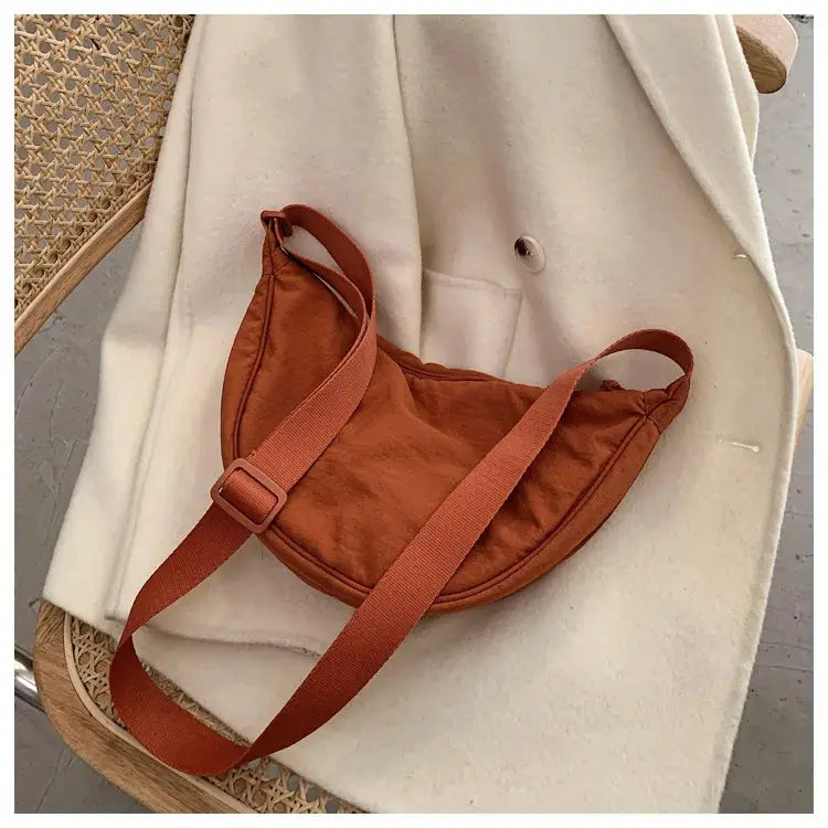 Casual nylon hobo crossbody bag in rust orange with adjustable strap on a cream coat