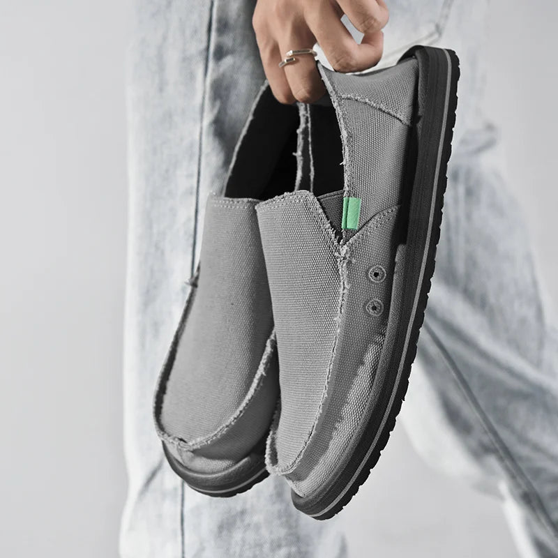Pair of grey canvas slip-on sneakers with frayed edges and black sole
