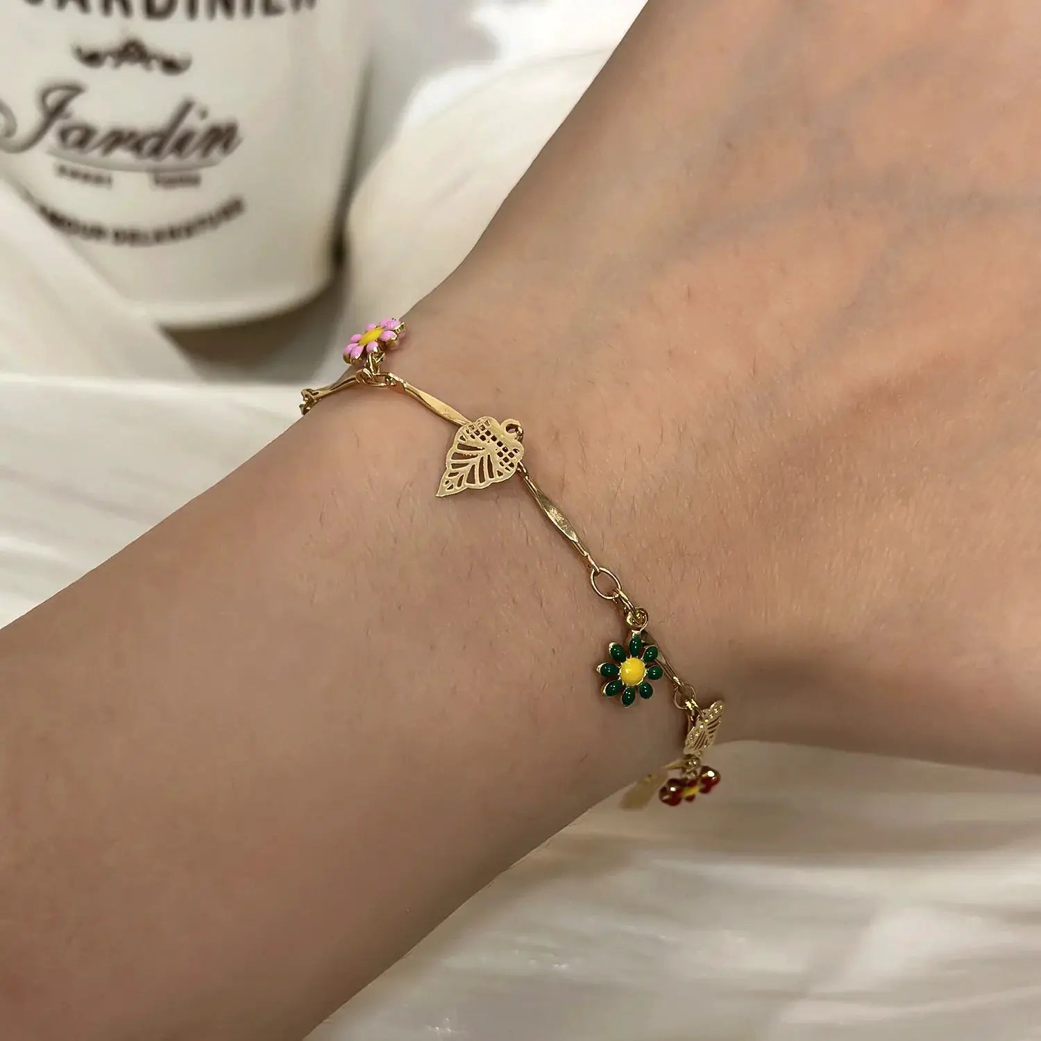 Gold-tone daisy flower bracelet with pink charm and leaf filigree accent