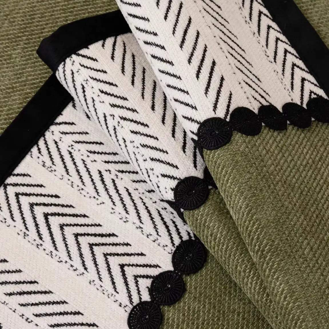 Sofa cover in white chenille with black chevron pattern over olive green twill, edged with black circular trim accents.