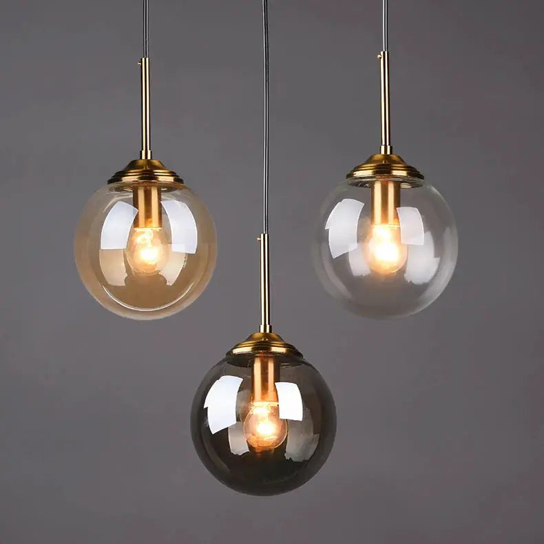 Modern luxury brass-tone metal chandelier with three glass globe pendant lamps (LED) for living and dining.