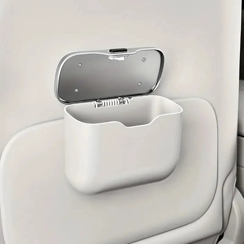 White plastic hanging car trash can with hinged lid, mounted on the back of a car seat.