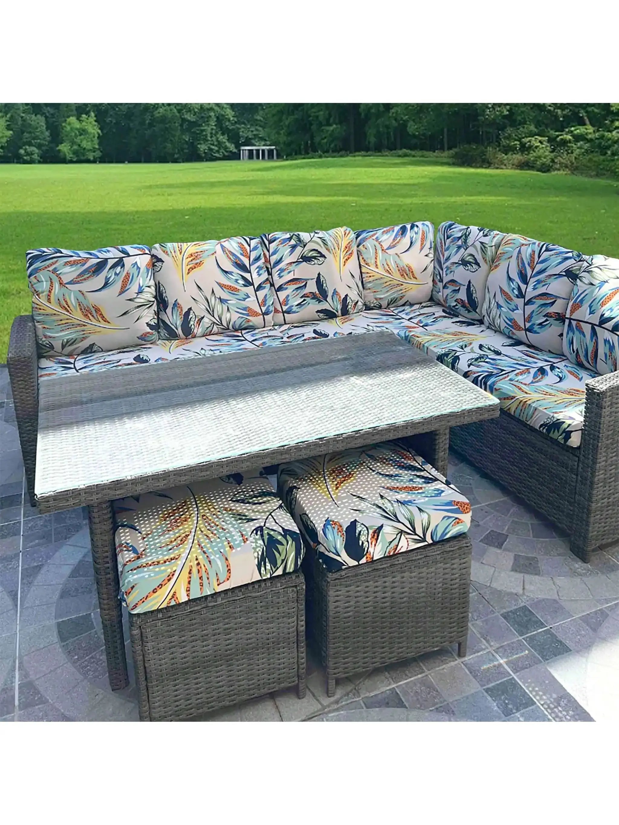 Outdoor tropical leaf print sofa cushions on a grey wicker sectional in a garden setting