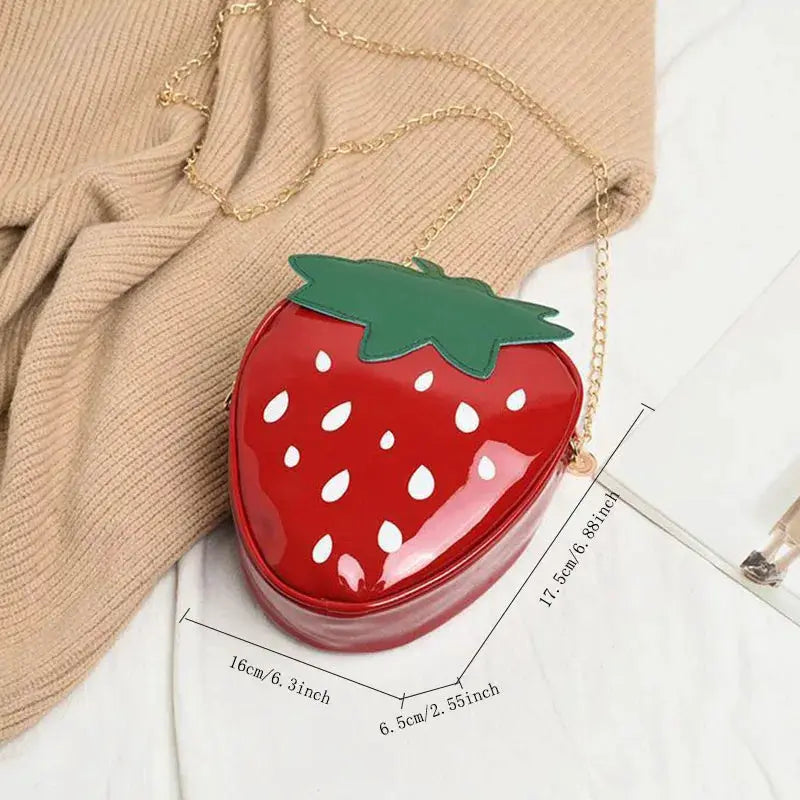 Strawberry-shaped red crossbody bag with a green leaf top and a gold chain strap.