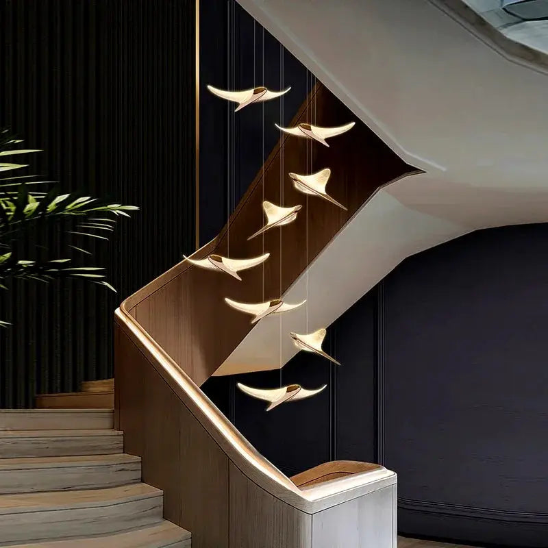 Seagull Staircase Pendant Lamp by Simples Market, gold-toned seagull-shaped pendants along a wooden staircase.