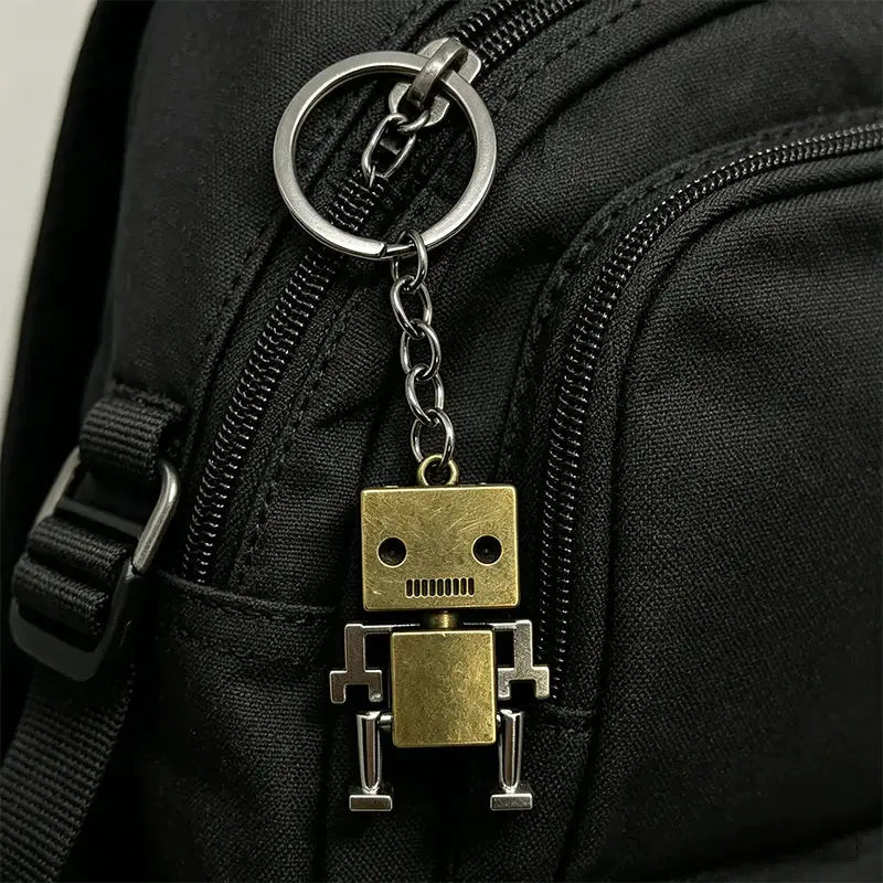 Retro movable robot keychain in brass-gold metal attached to a black backpack zipper