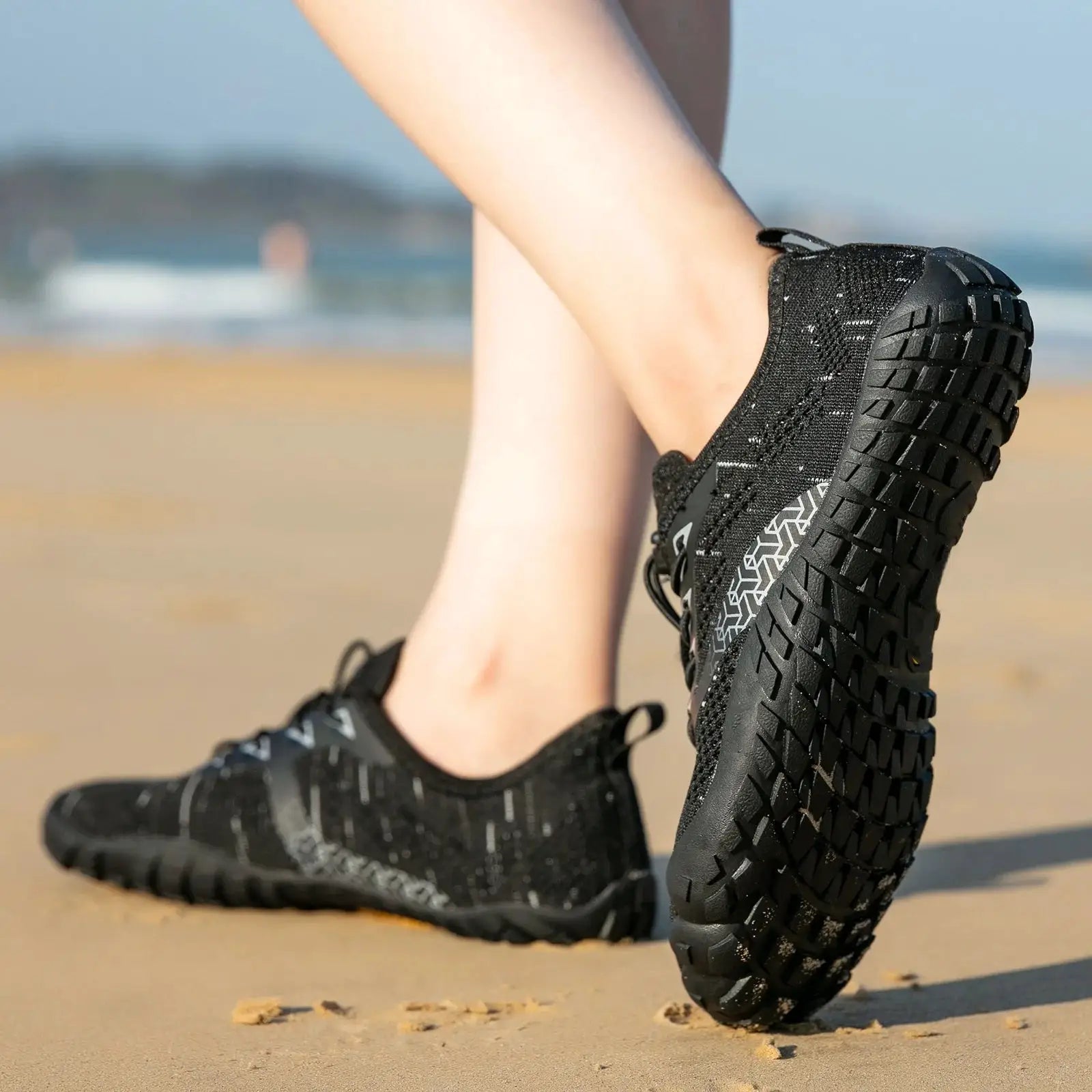 Men's trail running shoes, black minimalist barefoot design, wide width, zero-drop, on sandy beach.