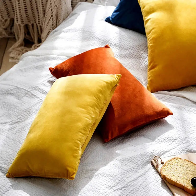 Four soft velvet cushions on a light sofa in mustard yellow, orange, and blue.