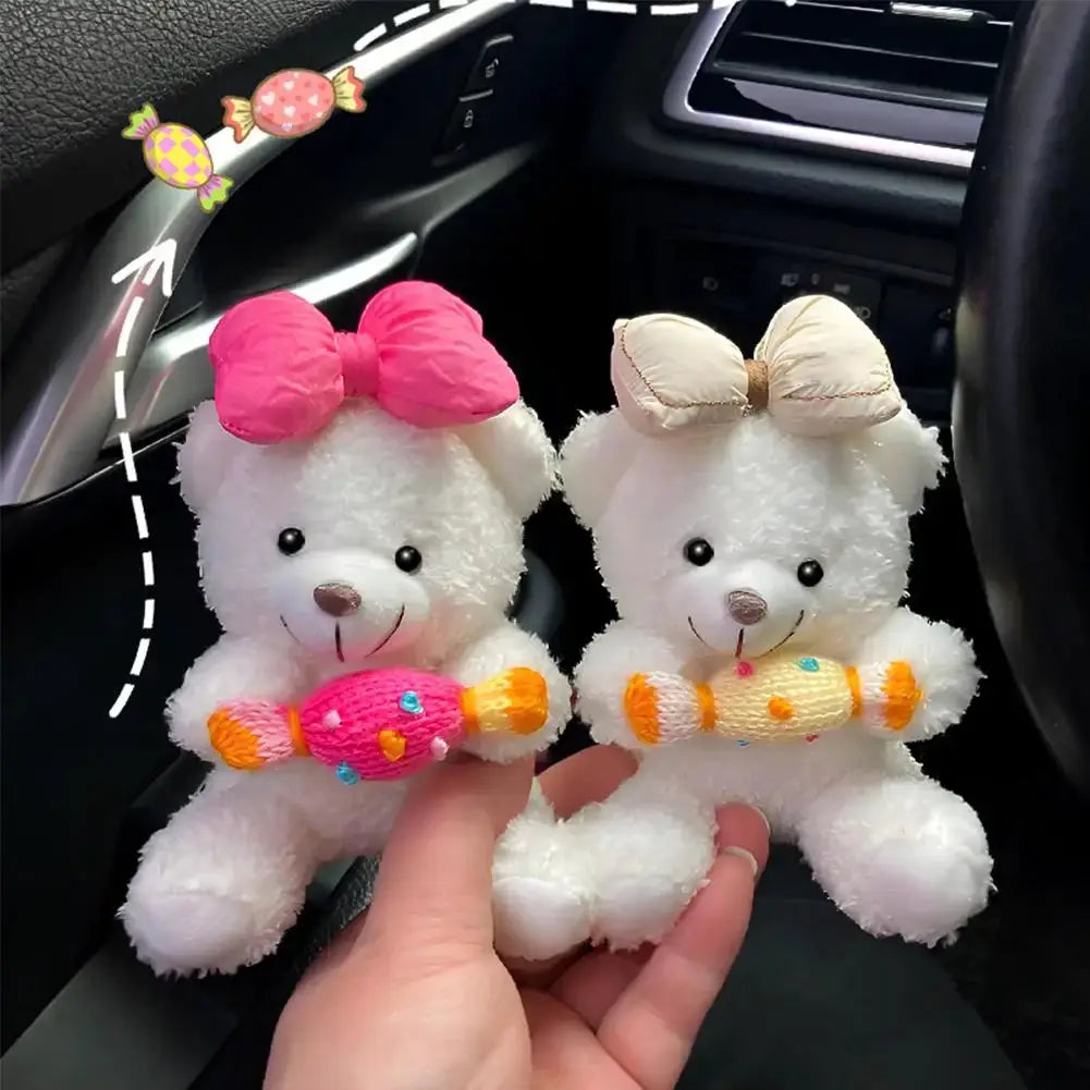 Two white plush Pilot Bear car ornaments with pink and beige bows, each holding a candy-shaped toy.