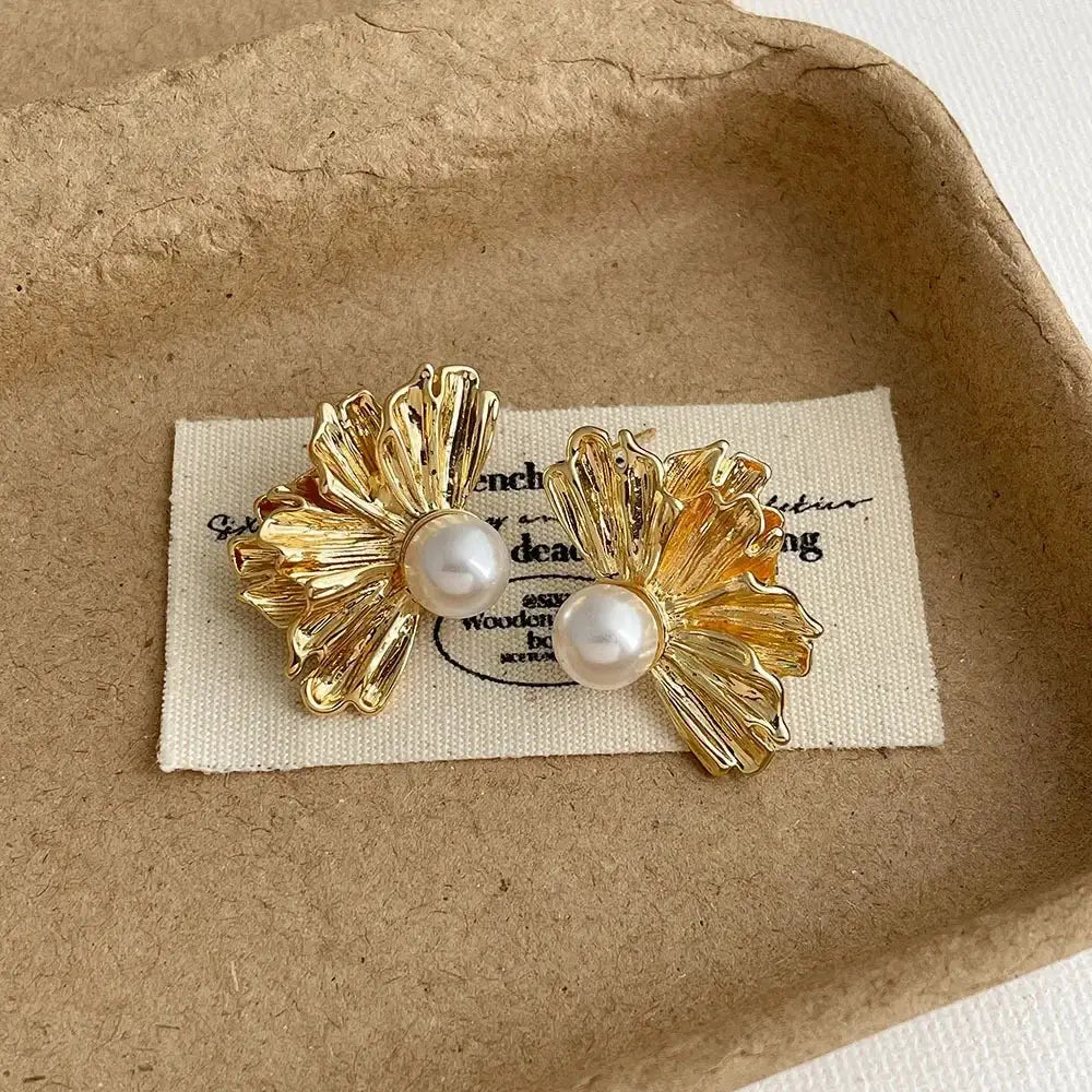 Pair of gold-tone shell texture stud earrings with pearl accents by Simples Market.