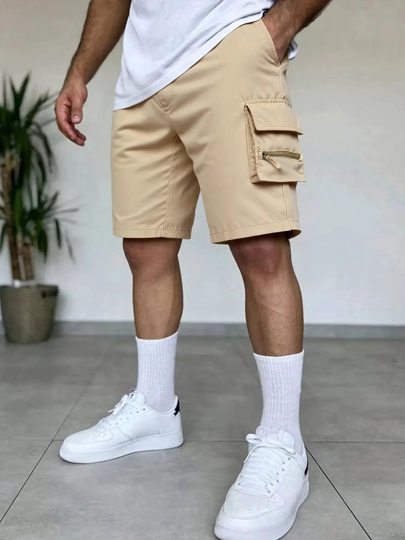 Beige men's cargo shorts with multiple pockets, including a side flap pocket and zip pocket
