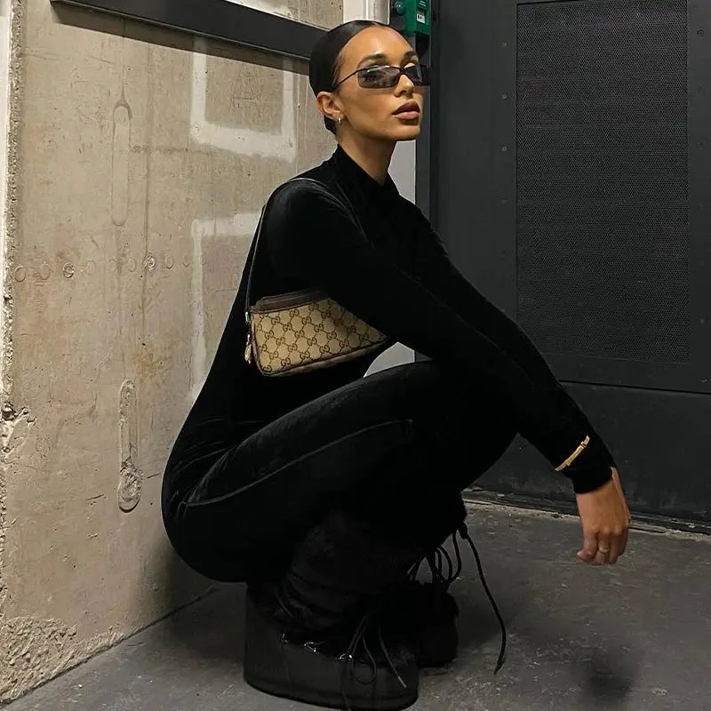 Black velvet Dulzura jumpsuit with long sleeves and O-neck, bodycon fit; Gucci monogram crossbody bag.