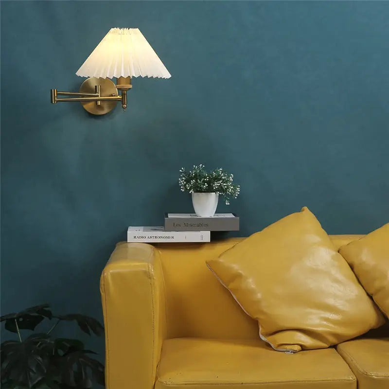 Nordic adjustable folding wall lamp with brass finish, pleated shade and LED light above a mustard leather sofa