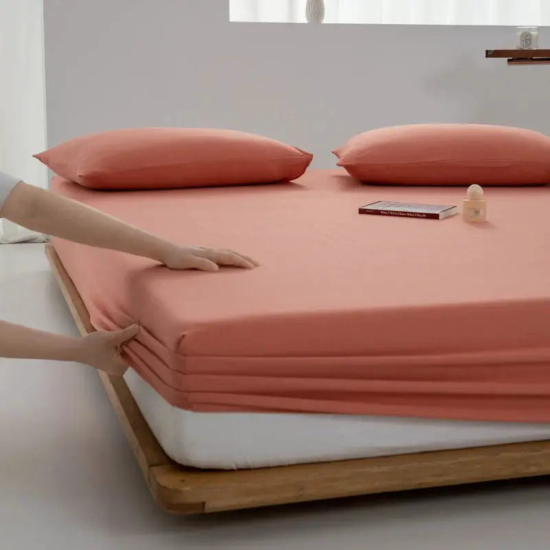 Soft cotton fitted sheet by Simples Market in peach pink with elastic edges; two matching pillowcases.