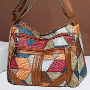 Women's crossbody shoulder bag in colorful patchwork geometric pattern with brown leather trim and multiple zip pockets