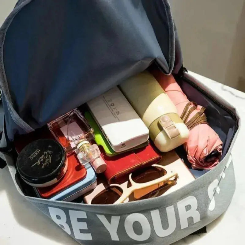 Gray fashion trend backpack, large-capacity unisex school bag shown open with cosmetics and sunglasses