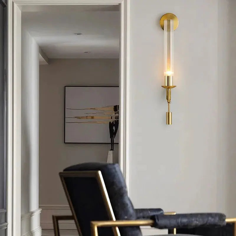 Modern copper wall sconce lamp with glass tube shade and brass finish mounted on a wall in a living room.