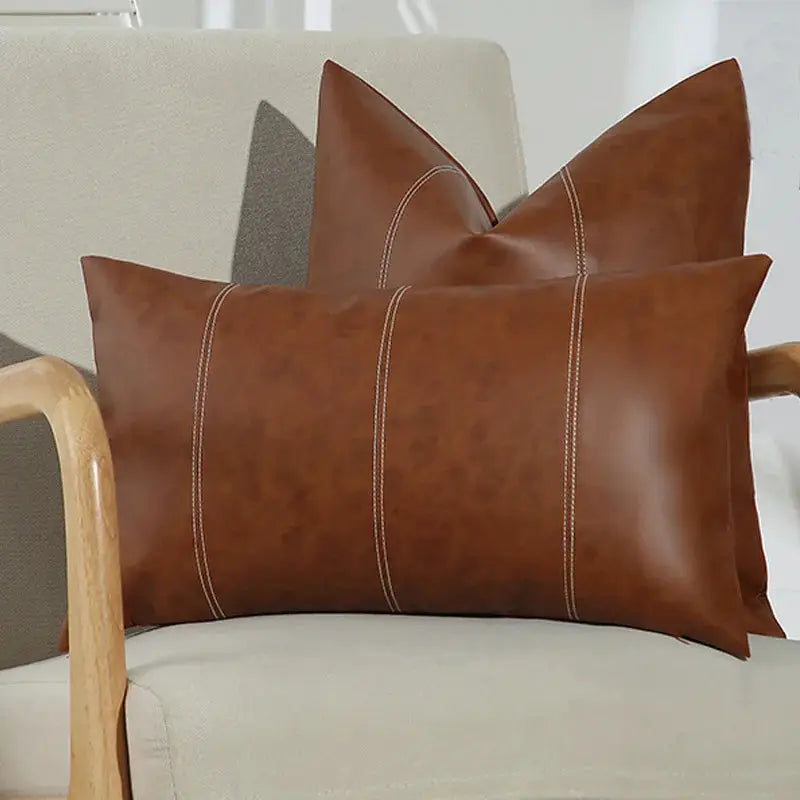 Two brown faux leather throw pillow covers with white contrast stitching, large decorative cushions for couch or bed.
