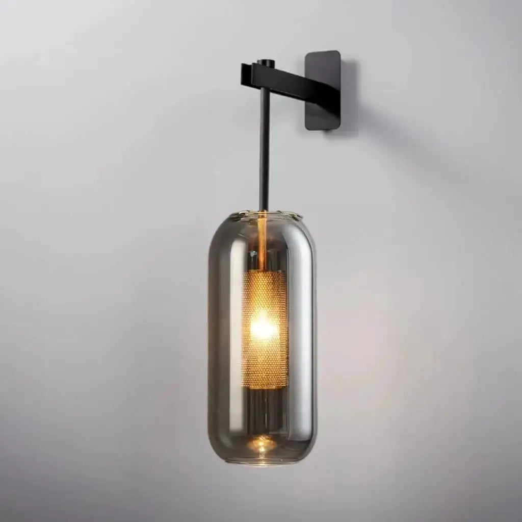 Modern glass wall light sconce with clear cylindrical shade, black mount and warm LED glow.