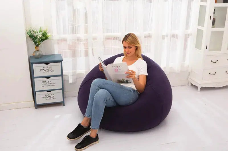 Purple inflatable sofa chair lounger, large PVC bean-bag couch; woman reads a magazine in a bright living room.