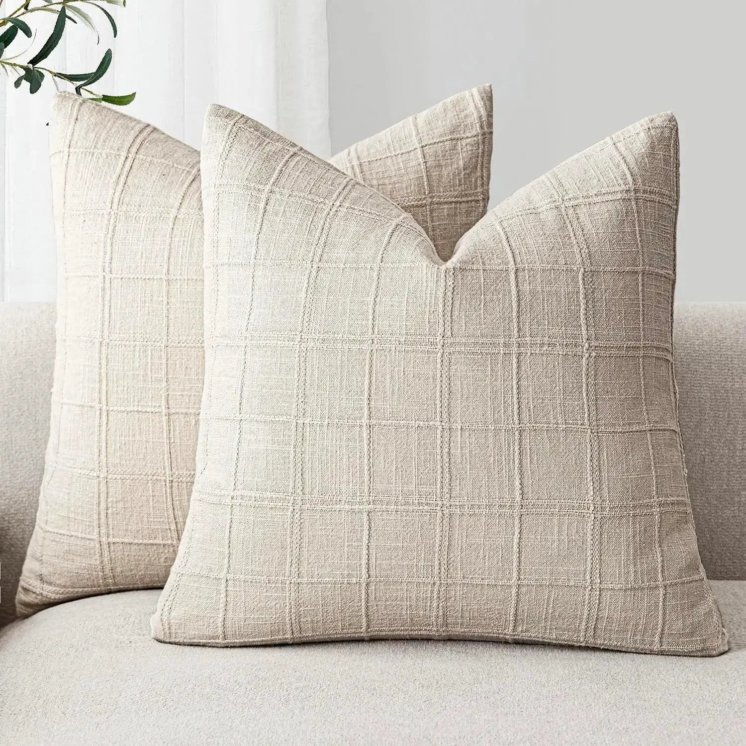 Beige square linen cushion covers; two decorative sofa pillows with a grid pattern on a light sofa