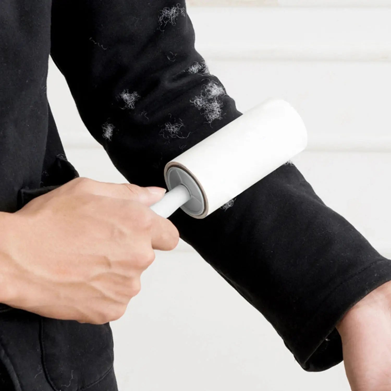Lint roller with refills by Simples Market; white roller on a handle removes pet hair from a black shirt sleeve.