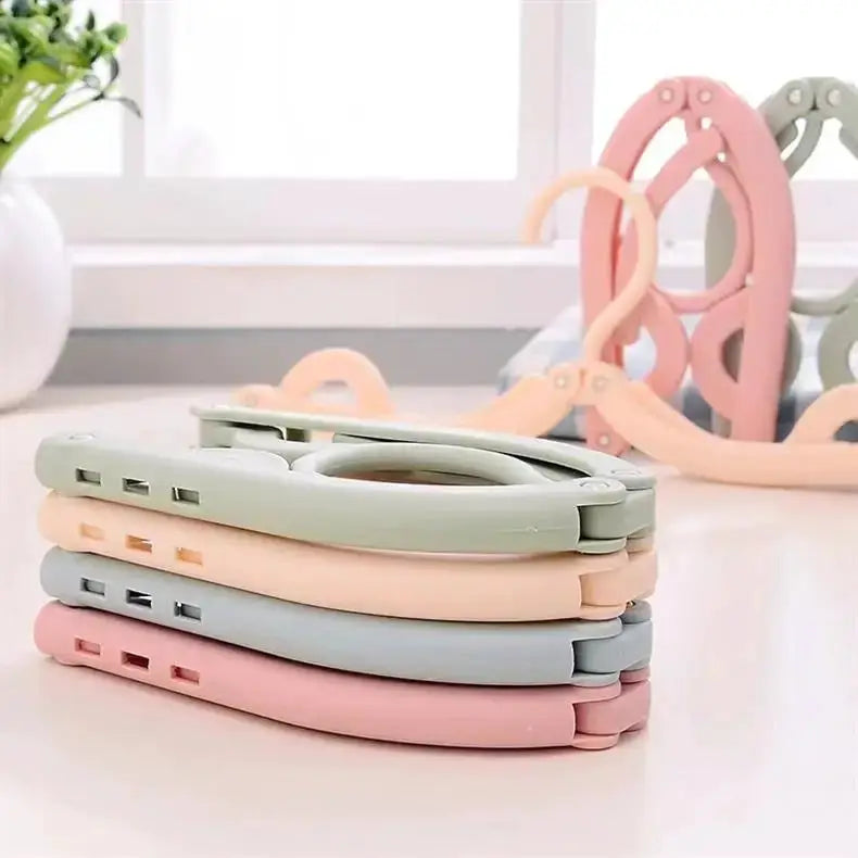 Foldable portable clothes hangers set in pastel green, peach, gray, and pink; ideal for travel and home storage.