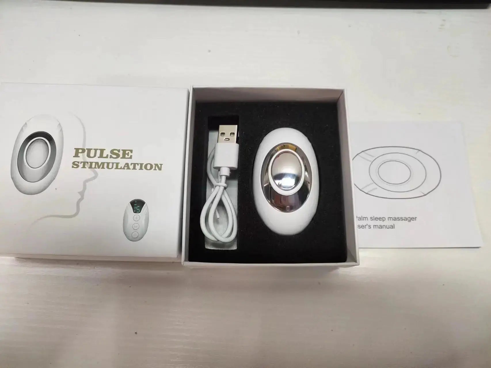 Simples Market sleep-aid handheld massager in white with a silver oval head, USB cable, and user manual.
