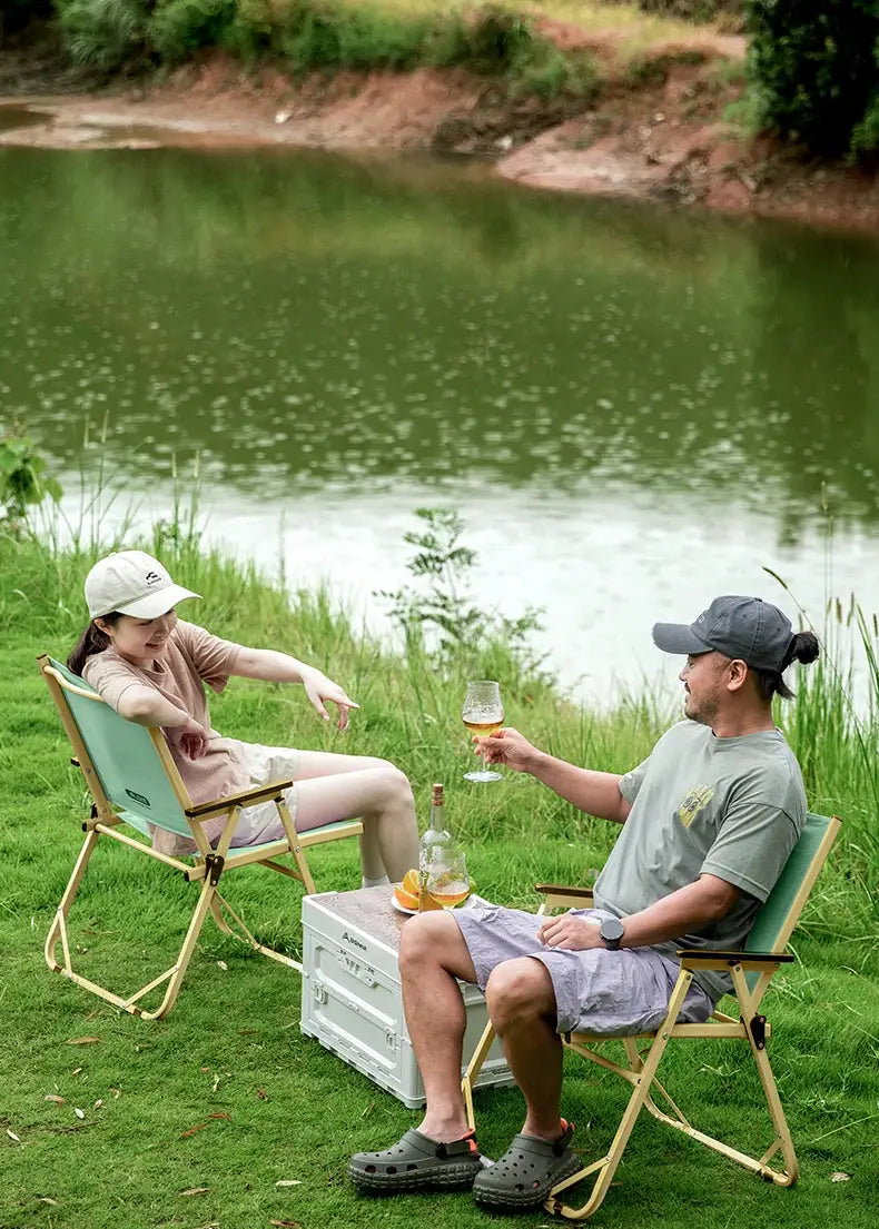 Two BISINNA outdoor folding camping chairs with light green fabric and beige frames by a lakeside picnic