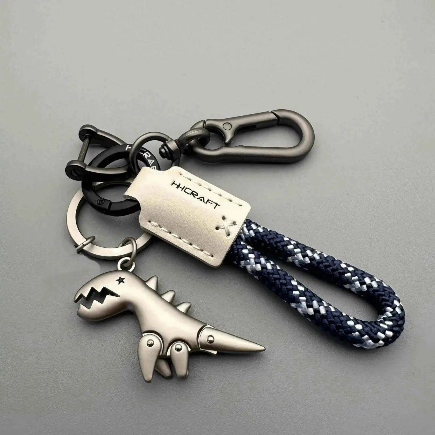 Keychain with HCraft leather tag and blue-and-white braided rope, metal dinosaur charm, carabiner clip