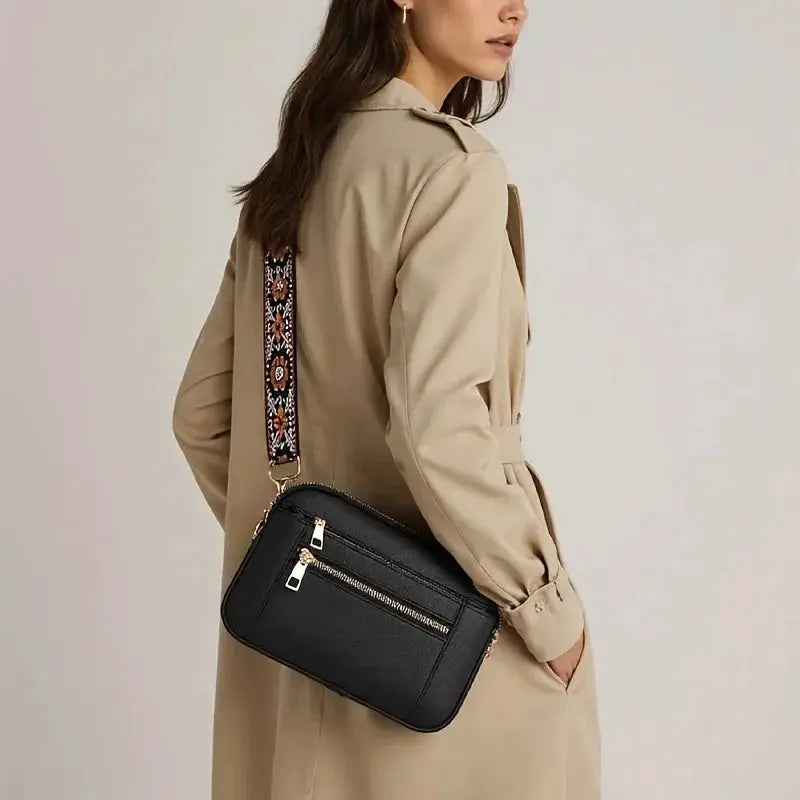 Crossbody bag in black, small square shape with front zipper pocket and patterned shoulder strap