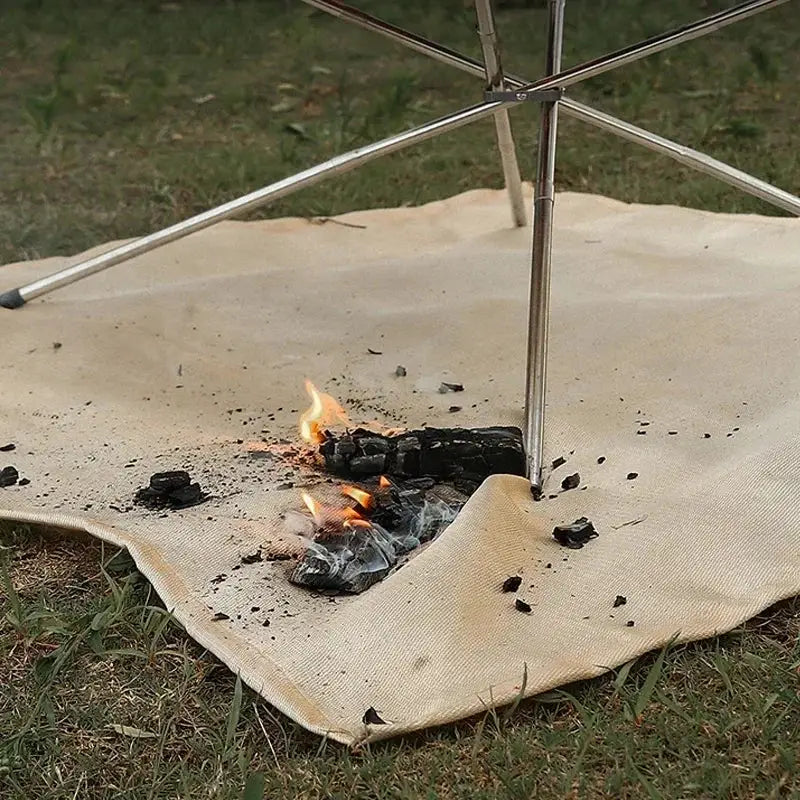 Simples Market fireproof fiberglass camping mat; beige insulated picnic ground cover under a metal frame with a small campfire.