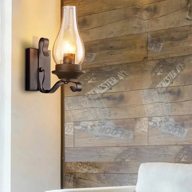 Wall lamp with glass hurricane shade and wrought-iron frame; black rustic industrial sconce.