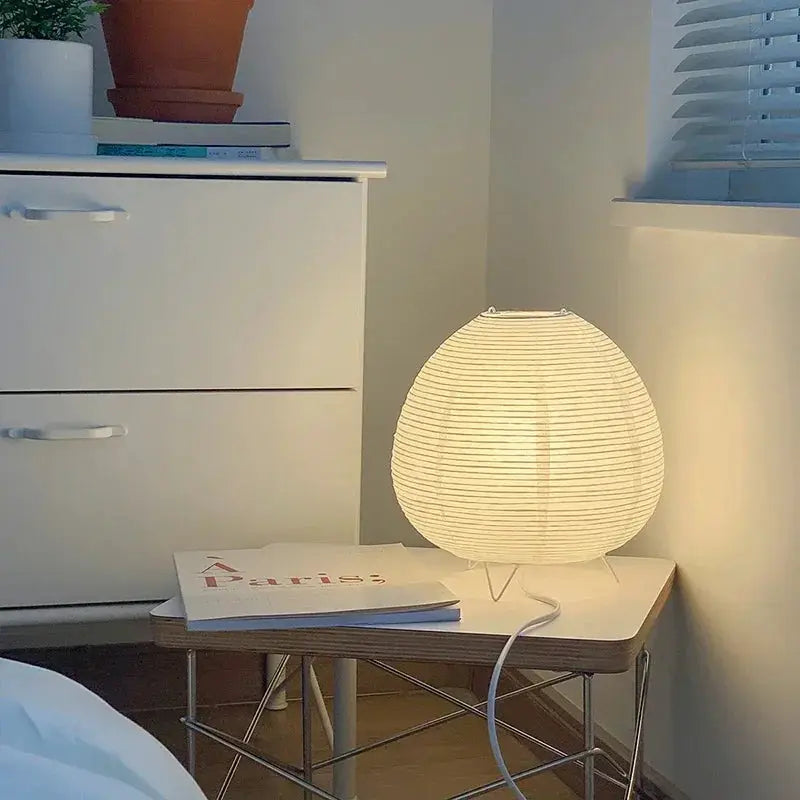 Japanese lantern LED table lamp by Simples Market with a rice paper shade on a white side table, warm ambient glow