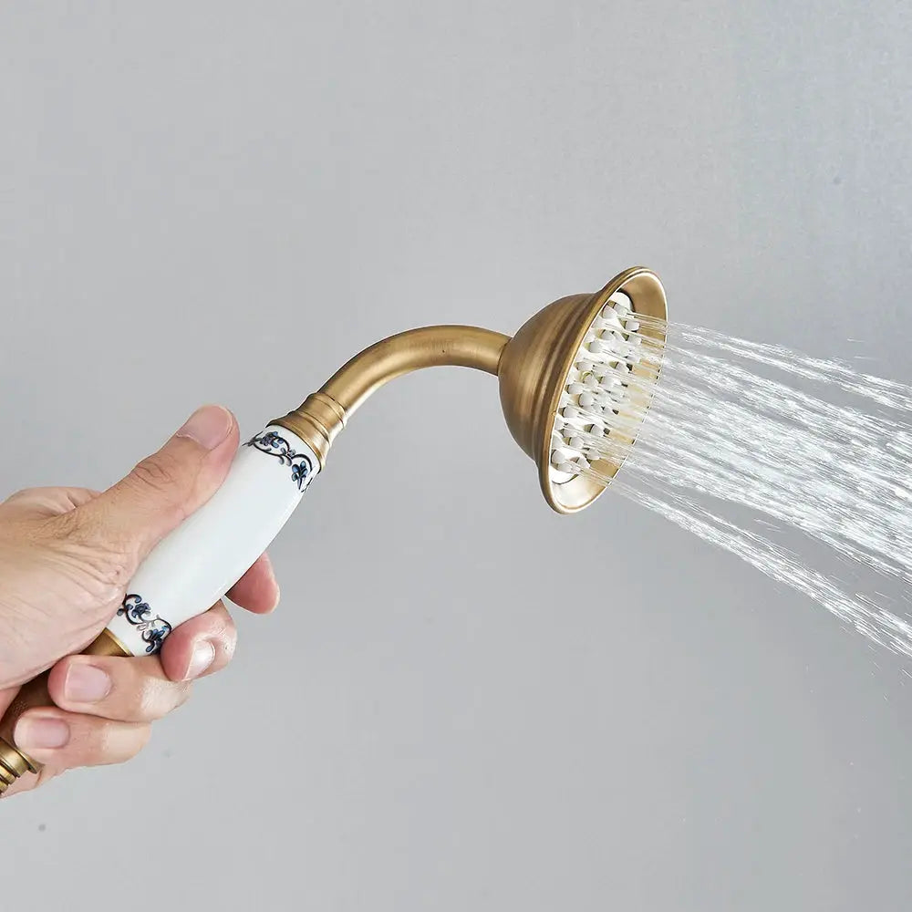 Antique brass handheld shower head with ceramic white handle by Simples Market, spraying water.