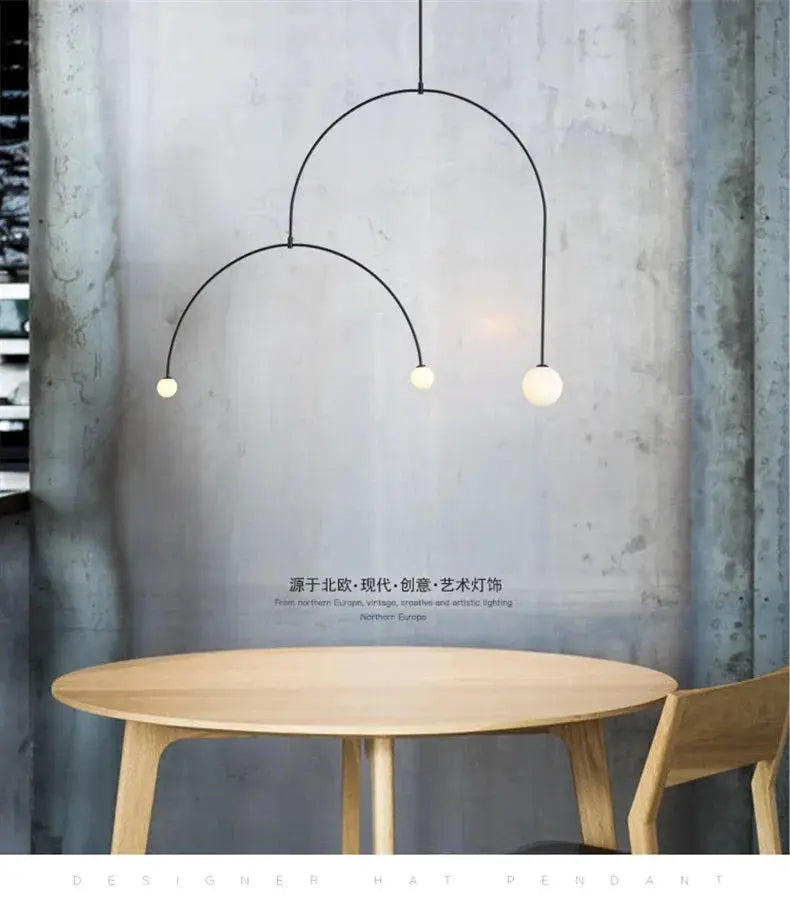 Nordic minimalist chandelier with three black metal arcs and globe bulbs mounted above a round wooden table.