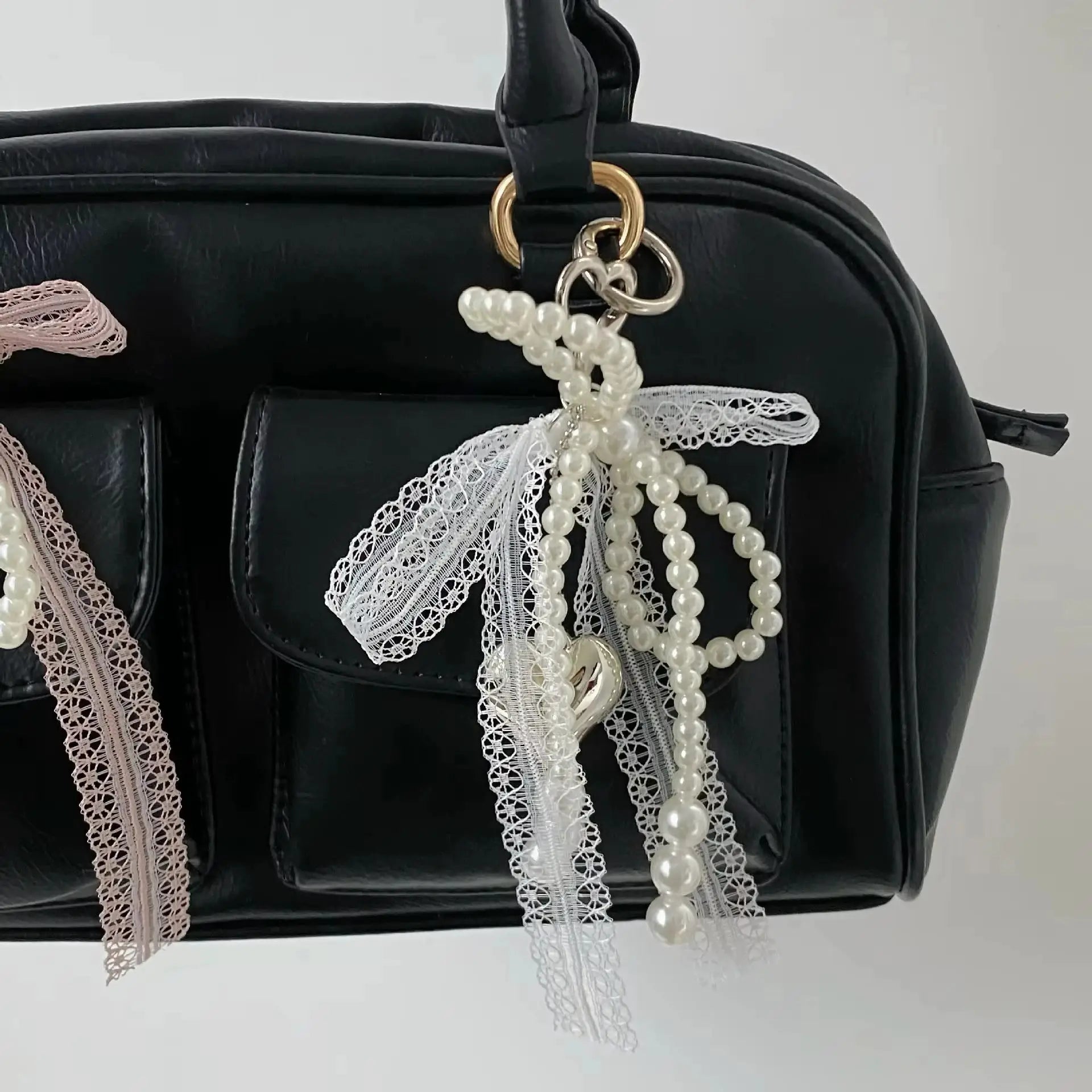 Pearl bead keychain with lace bowknot attached to a black handbag; white faux pearls with pink lace ribbon and gold ring.