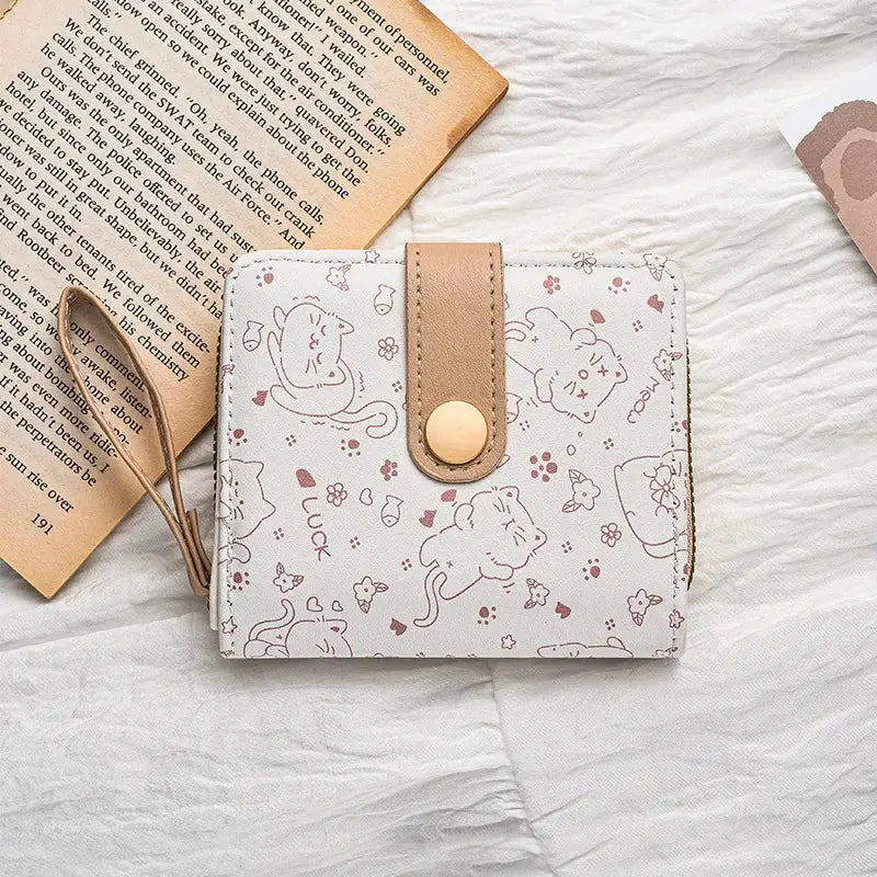 Wallet with white-pink cat print, brown faux-leather strap, gold snap, and zipper pocket with wrist strap