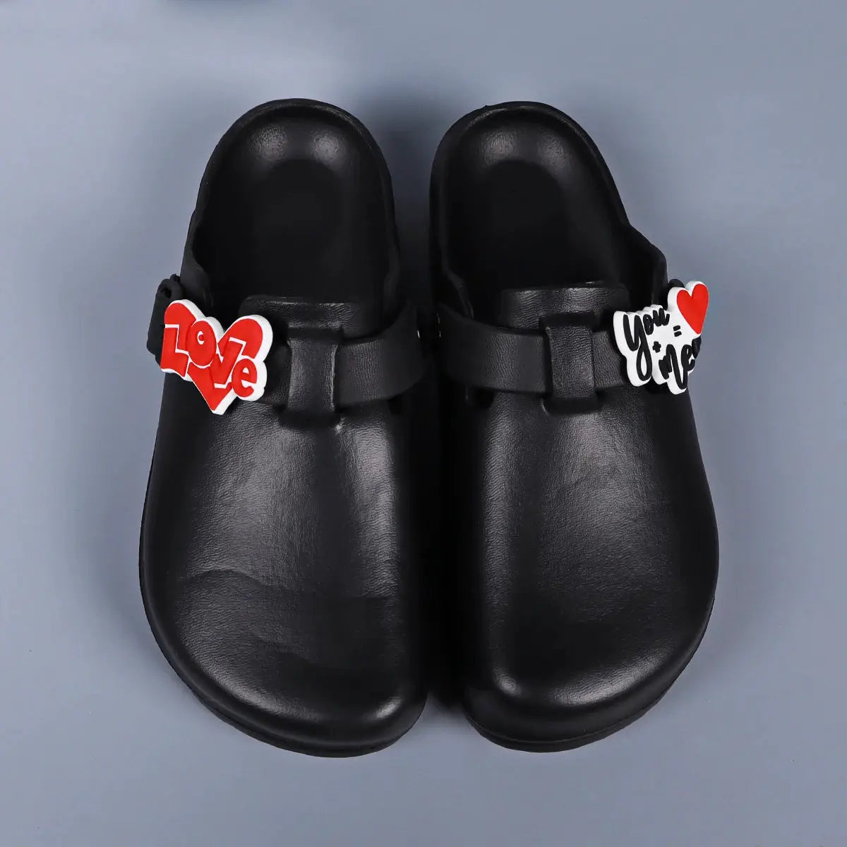 Pair of black EVA slides with heart charm decorations on straps, red Love and You & Me accents.