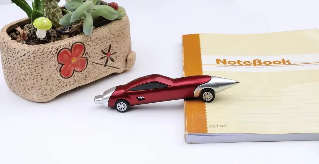 Car-shaped red ballpoint pen with candy color finish, kawaii stationery beside notebook