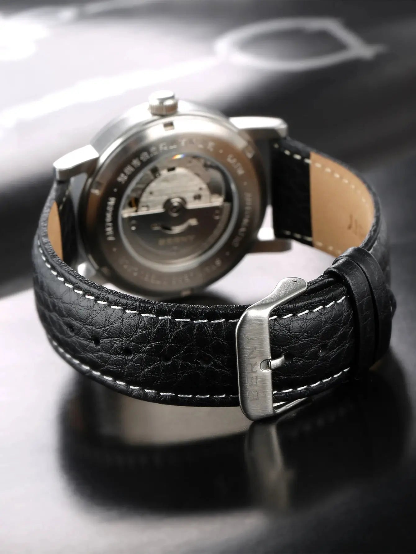 BERNY men's automatic wristwatch with black leather strap and silver case; transparent back reveals movement.
