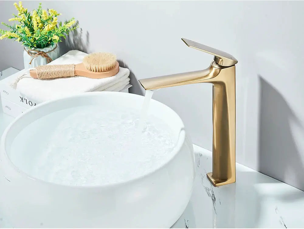 Brushed gold deck-mounted bathroom faucet with a single lever over a white ceramic sink.