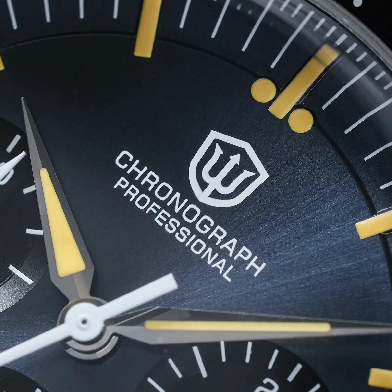 Chronograph watch dial close-up with black face, yellow luminous hands, white markers, shield logo