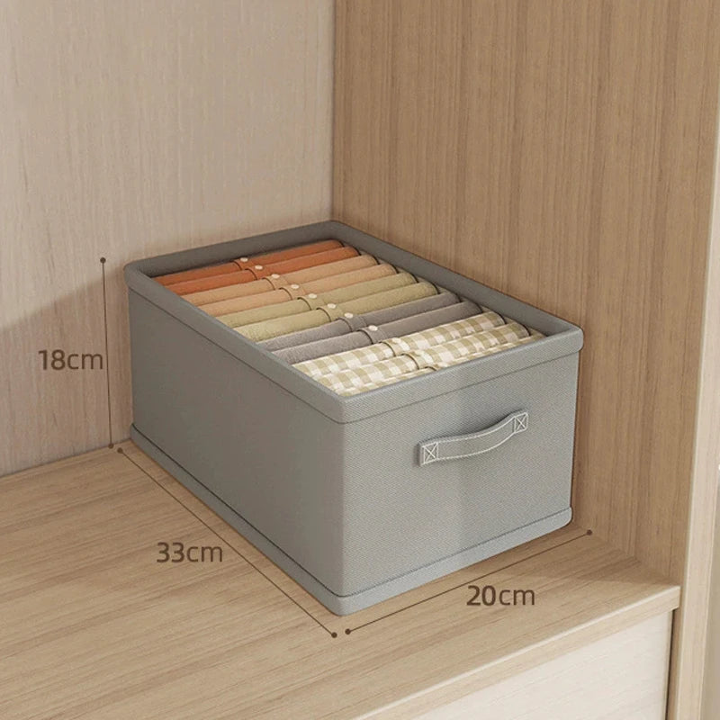 Clothes organizer storage box in gray fabric with several folded garments inside a wardrobe; 18×33×20 cm.