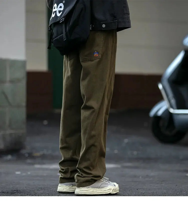 Japanese streetwear cargo pants for men in olive-brown with straight-leg fit and a small embroidered patch at pocket.